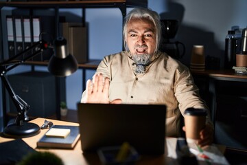 Sticker - Middle age man with grey hair working at the office at night doing stop gesture with hands palms, angry and frustration expression