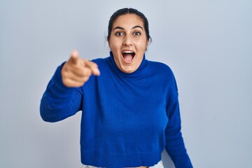 Poster - Young hispanic woman standing over isolated background pointing with finger surprised ahead, open mouth amazed expression, something on the front