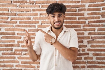 Wall Mural - Arab man with beard standing over bricks wall background pointing aside worried and nervous with both hands, concerned and surprised expression