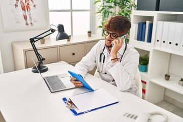 Poster - Young arab man wearing doctor uniform talking on smartphone using touchpad at clinic