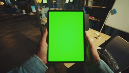 Close up hands man holding scrolling a vertical tablet computer with a green screen in the office. Mock-up display. Device. Apartment