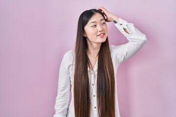 Poster - Chinese young woman standing over pink background smiling confident touching hair with hand up gesture, posing attractive and fashionable