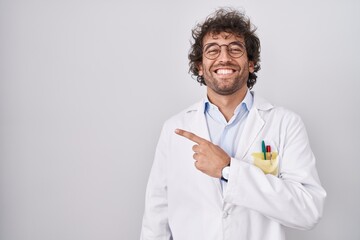 Wall Mural - Hispanic young man wearing doctor uniform cheerful with a smile of face pointing with hand and finger up to the side with happy and natural expression on face