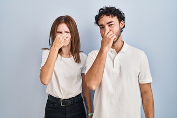 Canvas Print - Young couple wearing casual clothes standing together smelling something stinky and disgusting, intolerable smell, holding breath with fingers on nose. bad smell