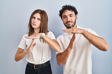 Poster - Young couple wearing casual clothes standing together doing time out gesture with hands, frustrated and serious face