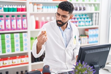 Sticker - Young arab man pharmacist using computer holding pills bottle at pharmacy