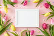 Top view photo of white photo frame yellow pink tulips and small hearts baubles on isolated pastel pink background. Happy Mother's Day concept