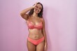 © Krakenimages.com - Young hispanic woman wearing lingerie over pink background doing ok gesture with hand smiling, eye looking through fingers with happy face.