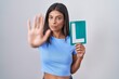 Brunette young woman holding l sign for new driver with open hand doing stop sign with serious and confident expression, defense gesture