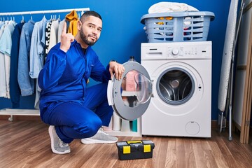 Wall Mural - Hispanic repairman working on washing machine surprised with an idea or question pointing finger with happy face, number one