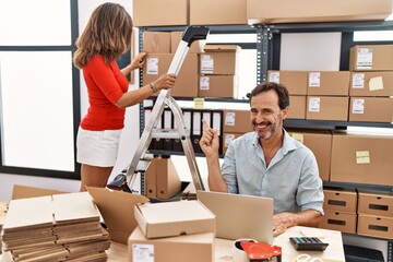 Canvas Print - Two middle age coworkers working at small business ecommerce smiling happy pointing with hand and finger to the side