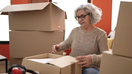 Poster - Middle age woman with grey hair unpacking cardboard box at new home