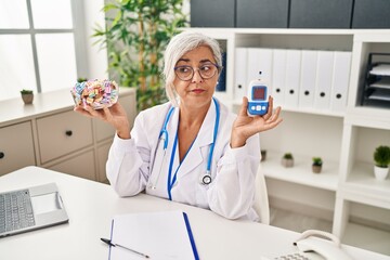 Poster - Middle age woman with grey hair wearing doctor uniform holding glucose monitor skeptic and nervous, frowning upset because of problem. negative person.