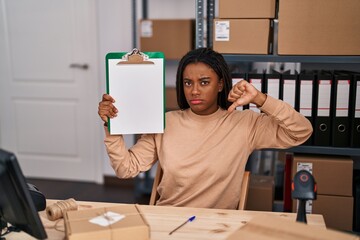 Poster - Young african american with braids working at small business ecommerce showing clipboard with angry face, negative sign showing dislike with thumbs down, rejection concept