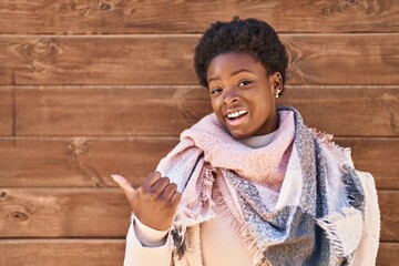 Poster - African american woman standing over wood background pointing thumb up to the side smiling happy with open mouth