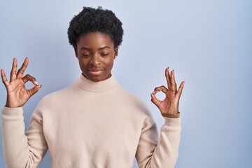 Canvas Print - African american woman standing over blue background relax and smiling with eyes closed doing meditation gesture with fingers. yoga concept.