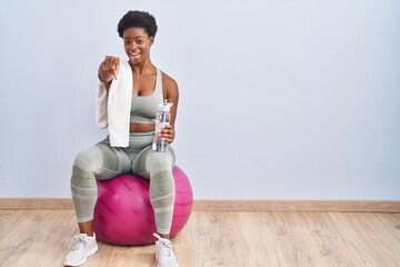 Wall Mural - African american woman wearing sportswear sitting on pilates ball pointing to you and the camera with fingers, smiling positive and cheerful