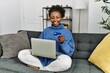 © Krakenimages.com - African american woman using laptop and credit card sitting on sofa at home