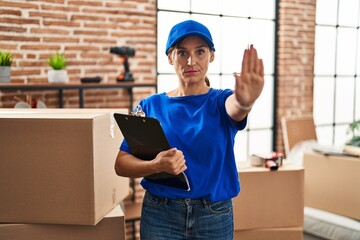 Sticker - Middle age brunette woman wearing delivery uniform at house moving with open hand doing stop sign with serious and confident expression, defense gesture