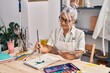 © Krakenimages.com - Middle age grey-haired woman artist smiling confident drawing on notebook at art studio