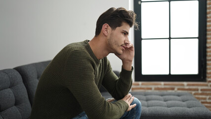 Wall Mural - Young hispanic man sitting on sofa with serious expression at home