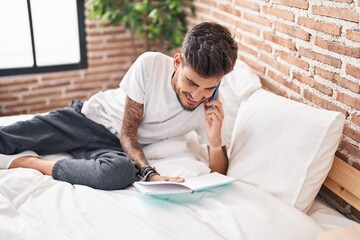 Sticker - Young hispanic man talking on smartphone writing on book at bedroom