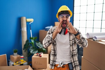 Canvas Print - Young hispanic man with beard working at home renovation shouting angry out loud with hands over mouth