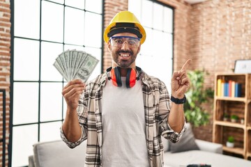 Sticker - Young hispanic man with beard working at home renovation holding dollars smiling happy pointing with hand and finger to the side