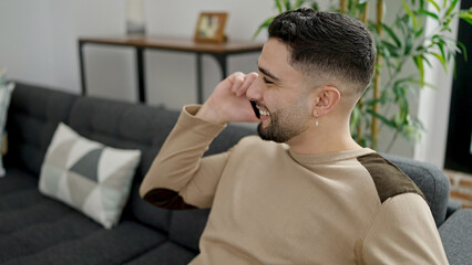 Wall Mural - Young arab man talking on the smartphone sitting on sofa at home