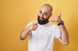 © Krakenimages.com - Young hispanic man with beard and tattoos standing over yellow background smiling doing talking on the telephone gesture and pointing to you. call me.