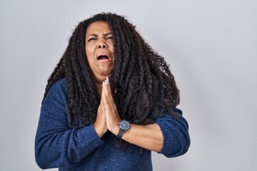 Wall Mural - Plus size hispanic woman standing over white background begging and praying with hands together with hope expression on face very emotional and worried. begging.