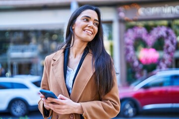 Wall Mural - Young hispanic woman smiling confident using smartphone at street