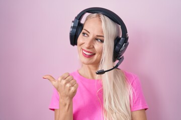 Poster - Caucasian woman listening to music using headphones smiling with happy face looking and pointing to the side with thumb up.