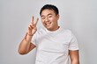© Krakenimages.com - Young chinese man standing over white background smiling looking to the camera showing fingers doing victory sign. number two.