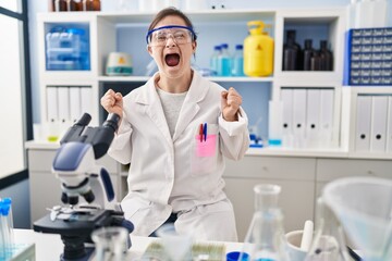 Poster - Hispanic girl with down syndrome working at scientist laboratory celebrating mad and crazy for success with arms raised and closed eyes screaming excited. winner concept