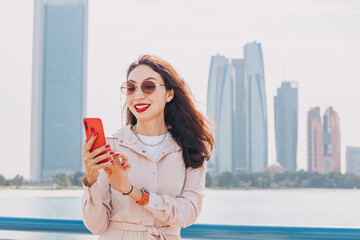 Wall Mural - Amidst the Abu Dhabi city towering skyscrapers, girl using a smartphone application to stay connected to the world around her. She remains glued to her phone, always 