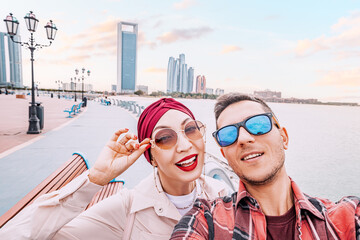 Adorable multicultural couple taking selfie photo on Abu Dhabi embankment with scenic view of skyscrapers in downtown