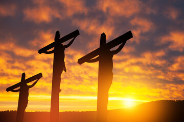Wall Mural - Silhouette of the crucified Jesus Christ on the cross along with other people on background of sunset sky.