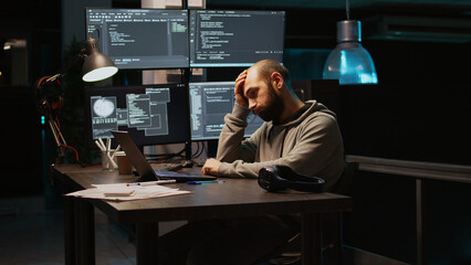 Young man feeling tired and working on programming code, typing database information and html script on laptop. Adult falling asleep at office, being exhausted using terminal window. Handheld shot.