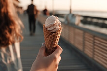 A Person Walking On A Boardwalk Or Pier While Holding An Ice Cream Cone With A View Of The Ocean Or Beach In The Background. Generative AI