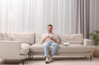 © New Africa - Happy man drinking coffee while resting on sofa near window with beautiful curtains in living room