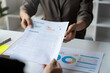 © Phimwilai - Accounting consultant, businesswoman handing in documents showing detailed information on graphs and data charts showing earnings, financial reports, income, taxes in the office.