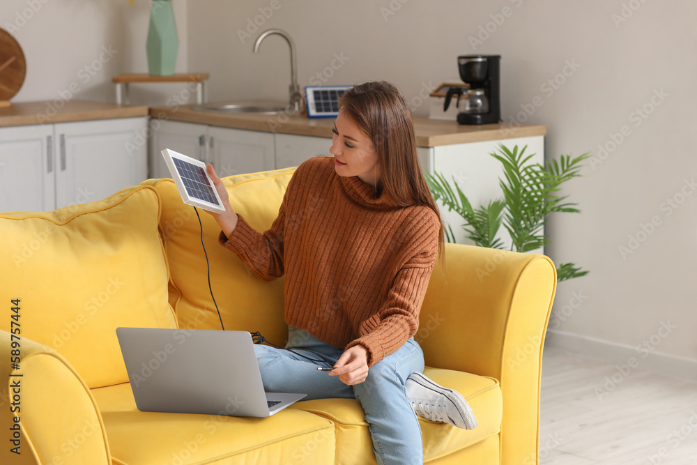 Pretty young woman charging laptop with portable solar panel at home