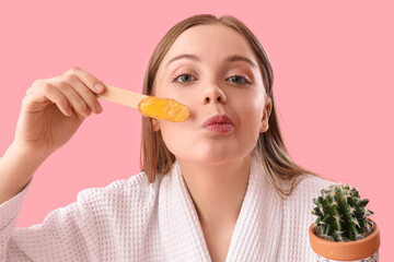 Wall Mural - Young woman holding spatula with sugaring paste and cactus on pink background