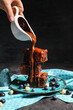 Woman pouring topping onto plate with pieces of tasty chocolate brownie on black background
