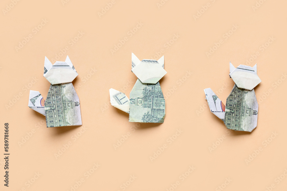 Origami cats made of dollar banknotes on beige background