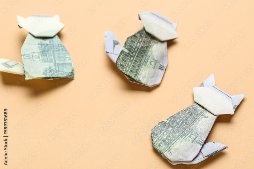 Origami cats made of dollar banknotes on beige background