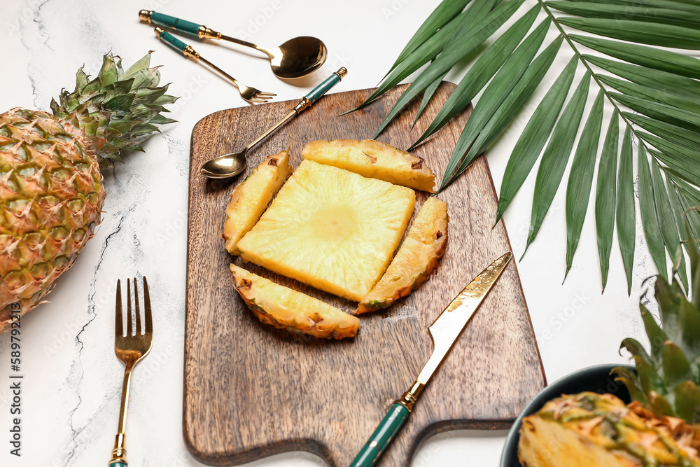 Wooden board with cut pineapple and palm leaf on light background