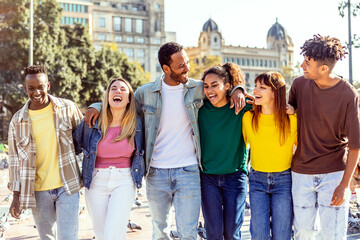 Wall Mural - Group of six multiethnic happy friends hugging each other walking in city street. United group of millennial people enjoying day off together. Multiracial friendship and community concept