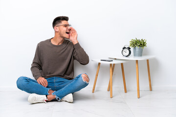 Wall Mural - Young caucasian man sitting in his home isolated on white background shouting with mouth wide open to the side